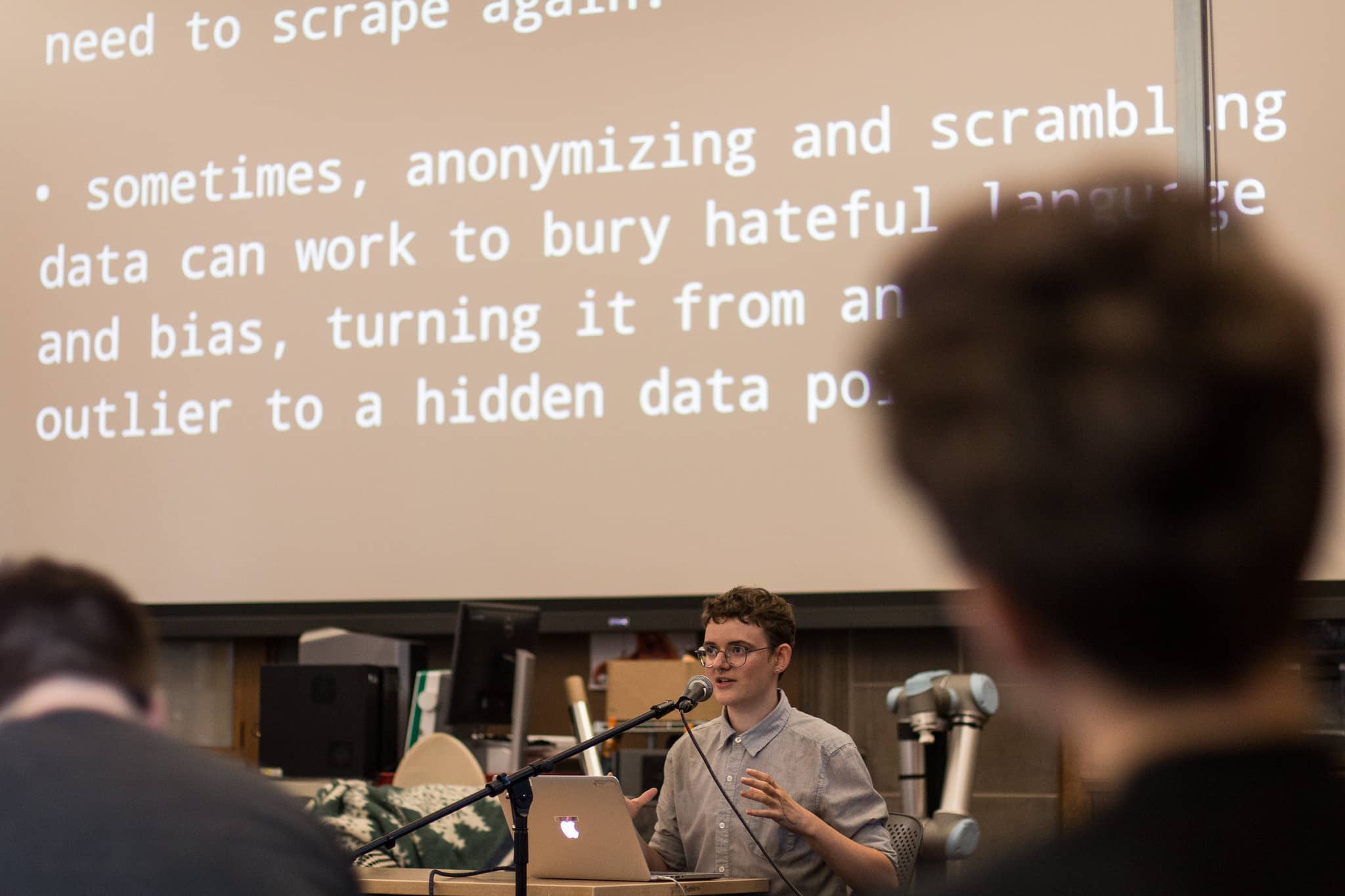 Participante en el podio habla frente a un texto proyectado sobre el problema de anonimizar datos "