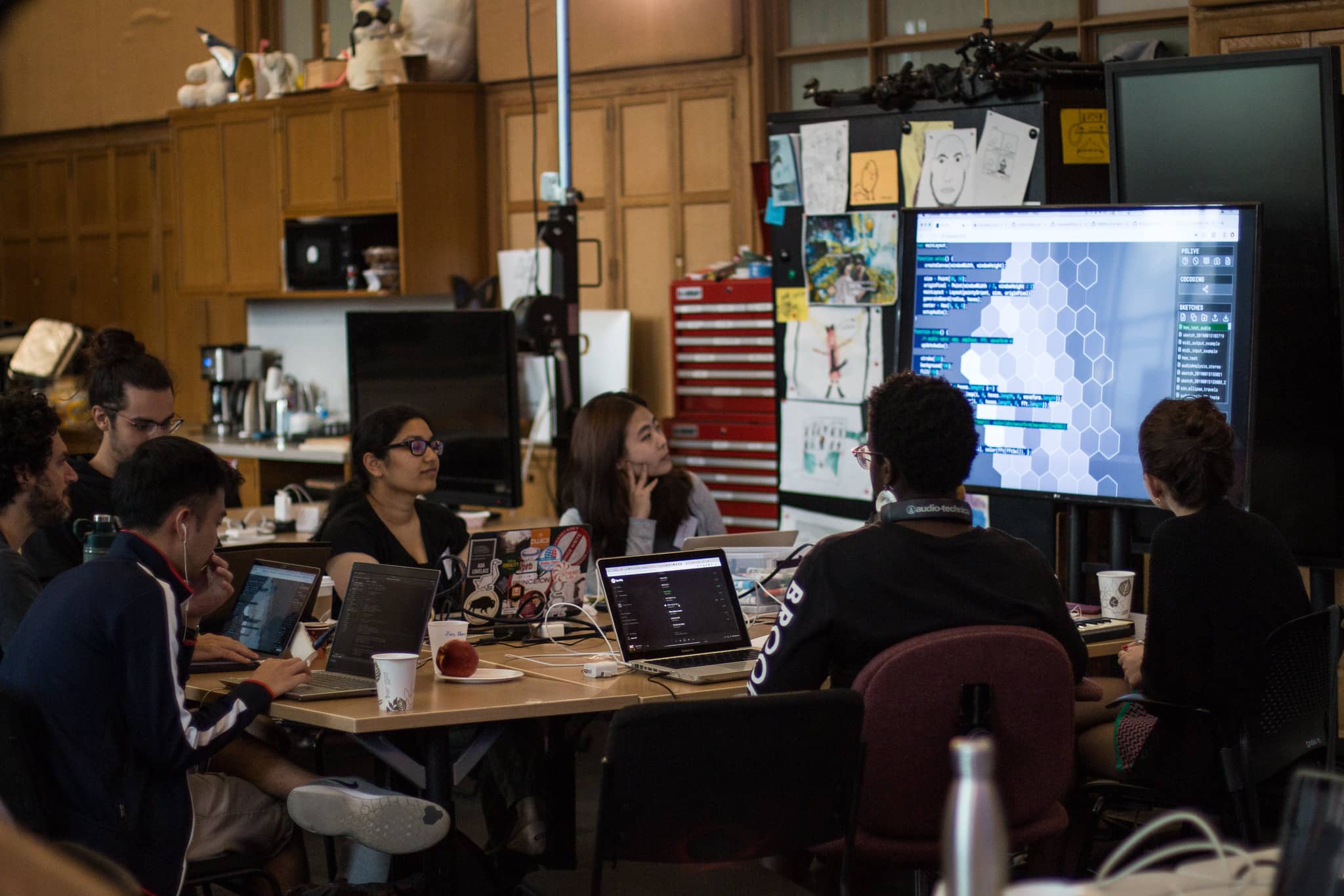 Participants sit around a table with their laptops and observe code on a screen