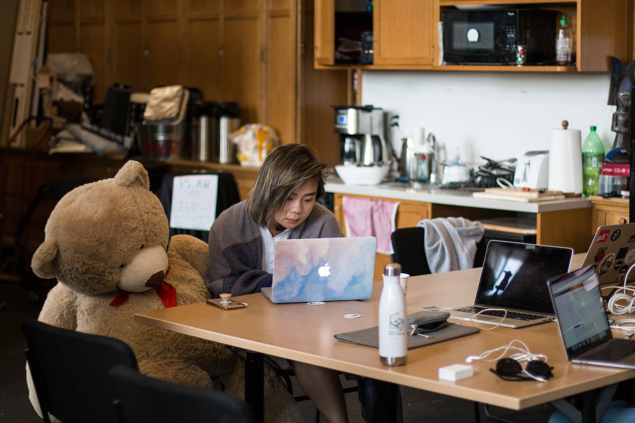 Woman sitting next to a lifesize teddy bear works on her laptop