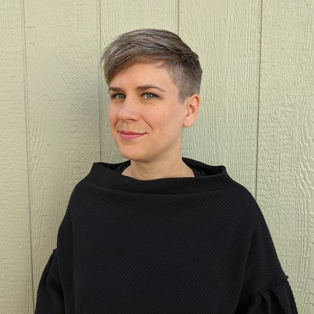 A photo of Kate. She is a light skinned person with short hair wearing a loose black shirt.