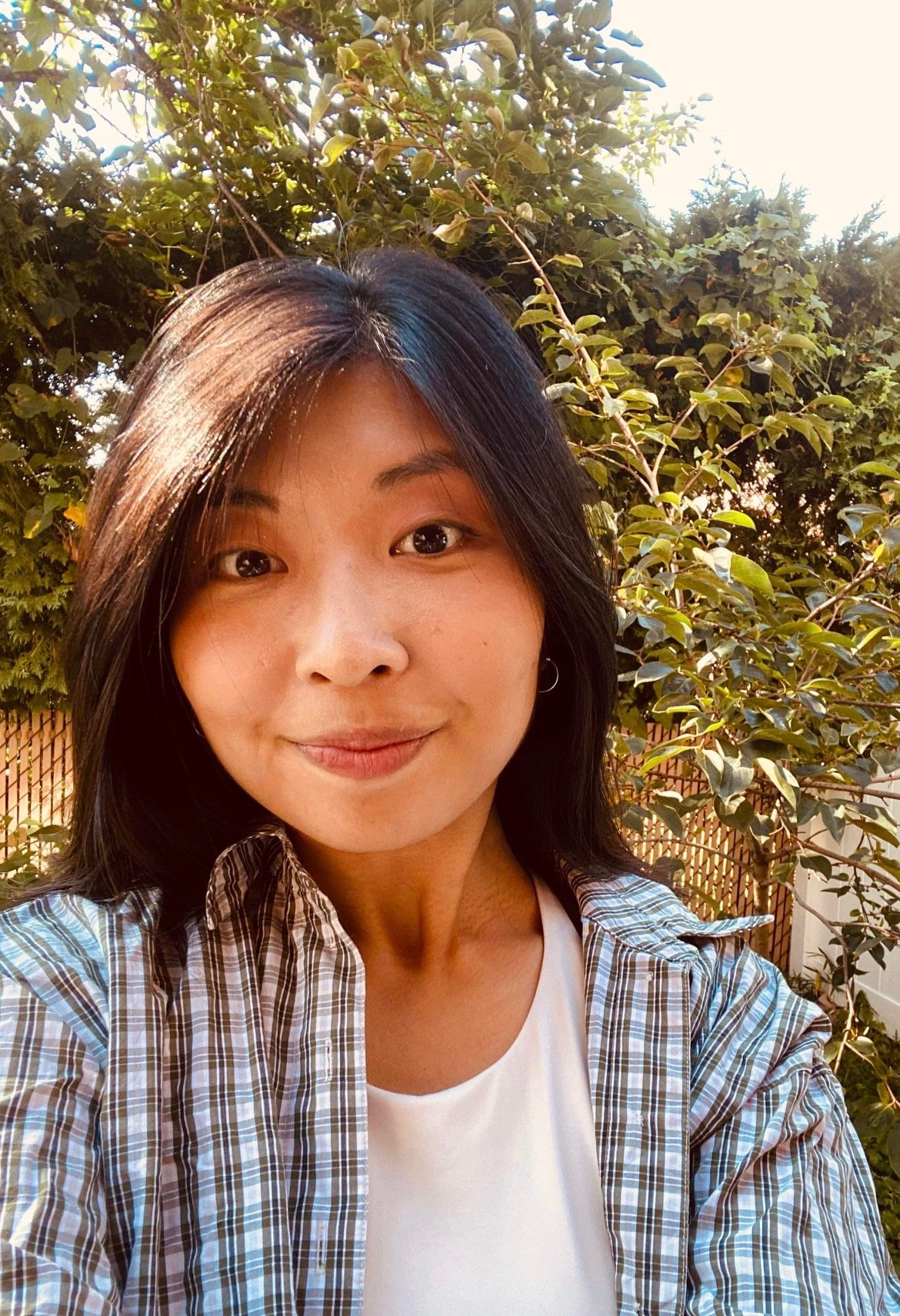 Rachel, a Korean-American woman with medium length black hair smiling as she stands in her backyard.