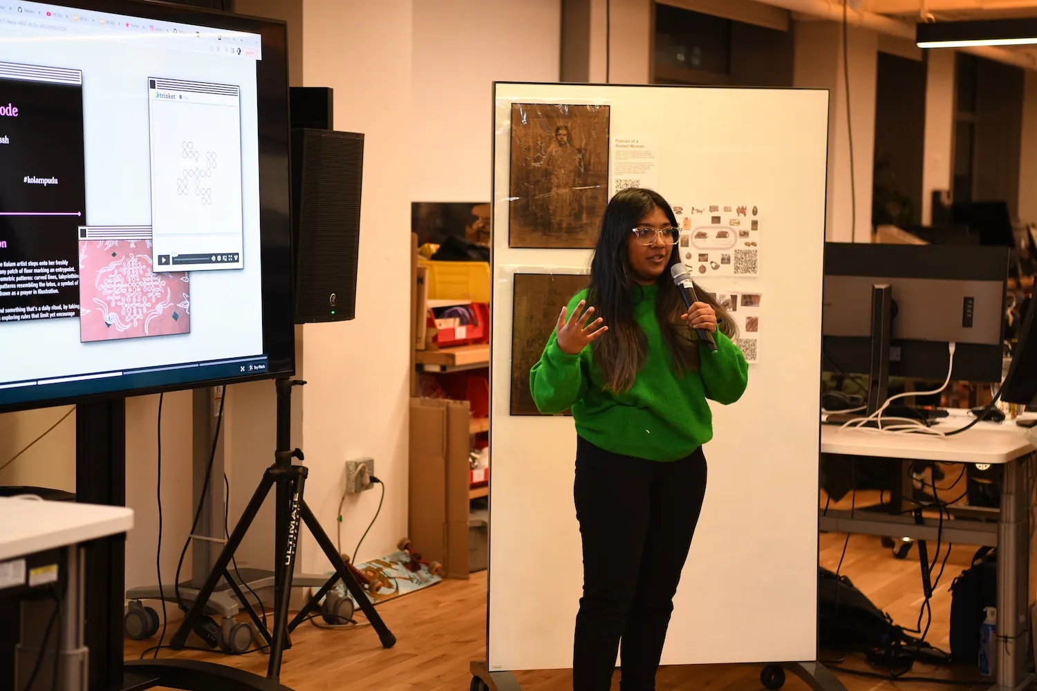 Lavanya Suresh holding a mic next to a big t.v. screen that has an image of her work on Kolams.